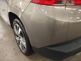 the rear end of a silver car in a garage with other cars in the background