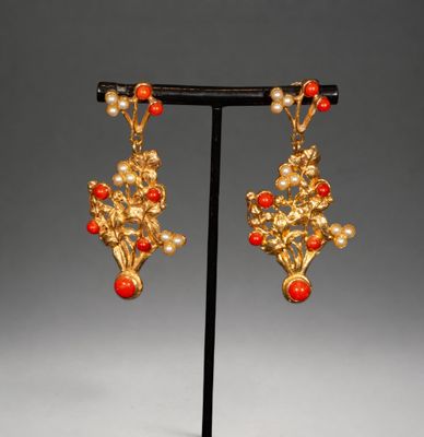 a pair of gold and coral earrings on a black stand