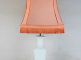 a white table lamp with a pink shade on top of it