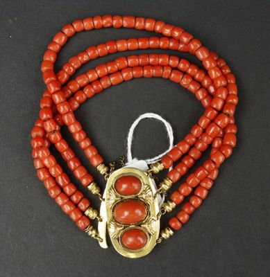 un gros plan sur un collier de perles rouges muni d'un fermoir doré