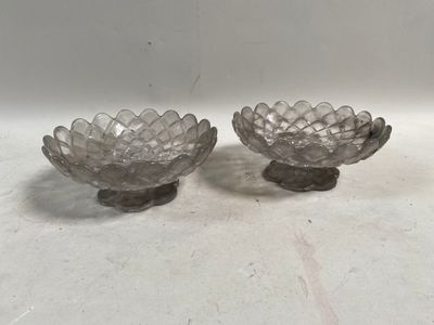 une paire de coupes à fleurs en verre transparent posées sur des socles, disposées sur une surface blanche