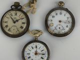three antique pocket watches are displayed on a white surface