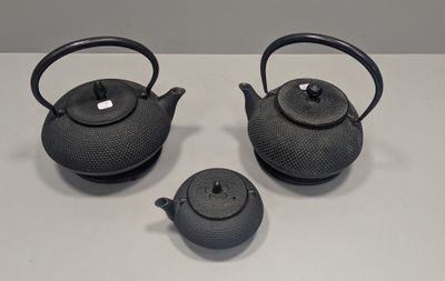 three black teapots sitting on a white table with a white background