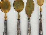 four spoons and a spoon with a gold handle are lined up on a white surface
