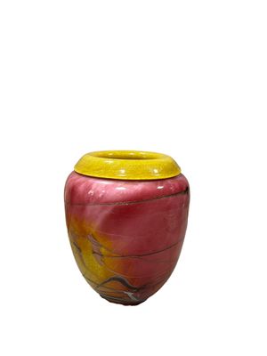 un vase rouge avec un couvercle jaune posé sur une surface blanche