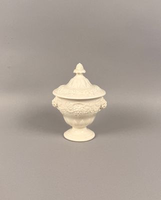urne en céramique blanche avec un couvercle, posée sur un support gris