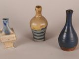 three different colored vases sitting next to each other on a white surface