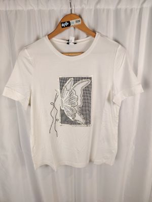 un t-shirt blanc orné d'un papillon, suspendu à un cintre devant un rideau
