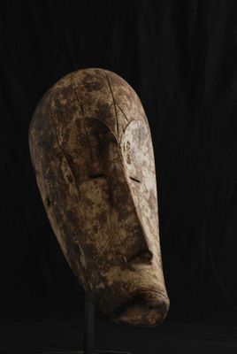 un gros plan d'un masque en bois posé sur un socle, sur fond noir