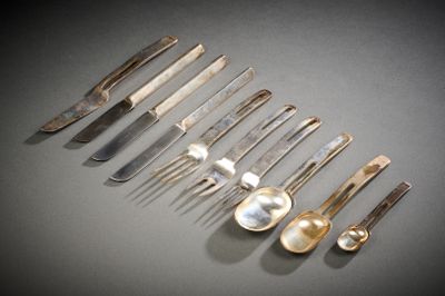Plusieurs cuillères, fourchettes et couteaux sont alignés sur une table