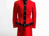 une veste et une jupe rouges, ornées de passementerie noire et de boutons, présentées sur un mannequin