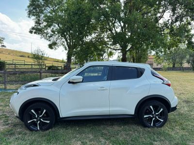 the white nissan juke suv is parked in a grassy field