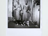 black and white photograph of two men standing next to each other in front of a curtain