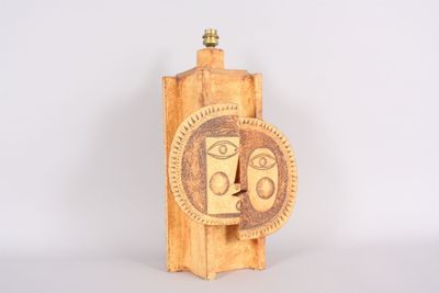 sculpture en bois représentant un visage, posée sur un socle en bois, avec un fond blanc