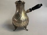 une cafetière en argent avec une poignée noire, posée sur une surface blanche