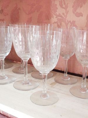 plusieurs verres à vin vides alignés sur une étagère devant un mur recouvert de papier peint