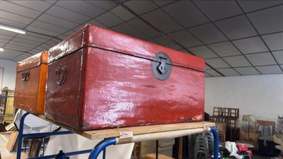 une malle rouge posée sur une charrette dans une pièce