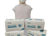 une personne portant un masque à côté de trois boîtes de masques jetables