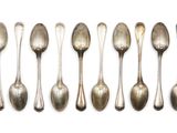 six cuillères en argent sont alignées sur une surface blanche