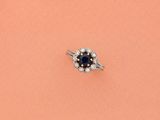 un gros plan d'une bague sertie d'un diamant et d'un saphir, posée sur un fond rose