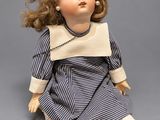 an old doll sitting on the ground wearing a blue and white striped dress