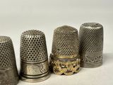 four antique thimbles lined up in a row on a white surface