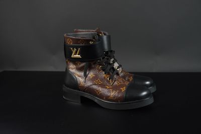 Des bottes Louis Vuitton posées sur une surface noire, sur fond gris