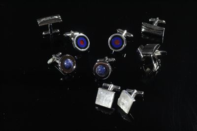 six paires de boutons de manchette ornées de pierres bleues et rouges sur un fond noir