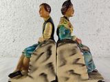 two figurines of people sitting on a rock on a white surface