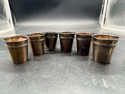 six verres à shot en laiton vieilli alignés sur une table