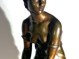 bronze statue of a woman sitting on a rock with her hands on her knees
