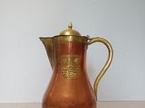 an antique copper coffee pot with a brass handle on a table