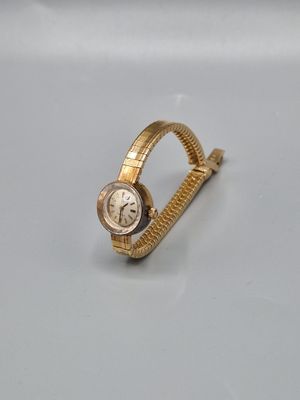 une montre en or posée sur une surface blanche