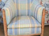 an old chair with a plaid upholstered seat in front of a floral wallpapered wall