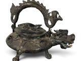 une vieille théière en bronze avec une anse en forme de dragon sur fond blanc