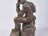 bronze statue of a man sitting on a rock with his head in his hands