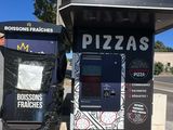 two machines that are sitting outside of a pizza shop