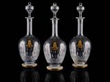 trois bouteilles en verre transparent ornées de touches dorées, posées sur un fond noir