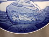 a blue and white plate with a picture of a woman on a rock