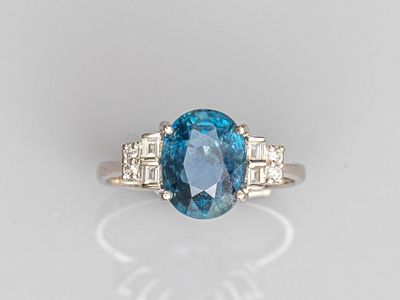 a close up of a blue diamond and diamond ring on a white surface