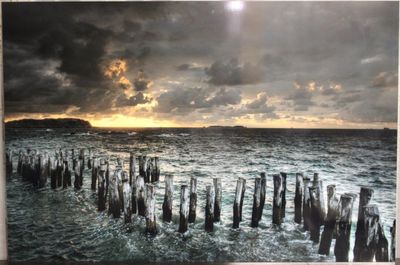 tableau représentant un coucher de soleil sur un plan d'eau, avec des poteaux en bois au premier plan