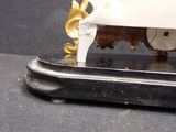 a white and gold clock on a stand on a black surface