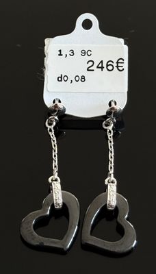 une paire de boucles d'oreilles noires en forme de cœur suspendues à une étiquette posée sur une surface noire