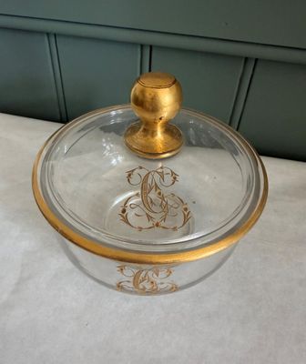 un saladier en verre avec un couvercle doré posé sur une table