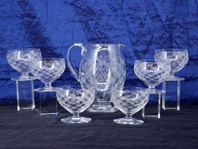 six glasses and a pitcher sitting on a table