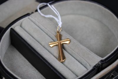 une petite croix en or dans un écrin, accompagnée d'un cordon blanc