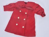 un manteau rouge de poupée orné de boutons blancs, posé sur une surface blanche
