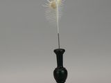 a white feather on top of a black vase