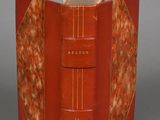 an old book with a red cover sitting on top of a table