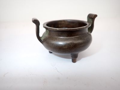 un petit pot en bronze muni d'une anse, posé sur une surface blanche